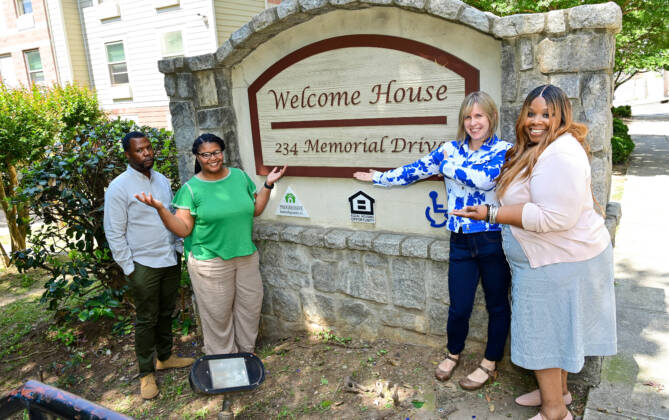 3Keys staff and residents stand in front of the sign for Welcome House, an apartment complex for those in Atlanta experiencing homelessness. Photo credit: Kimberly Evans.